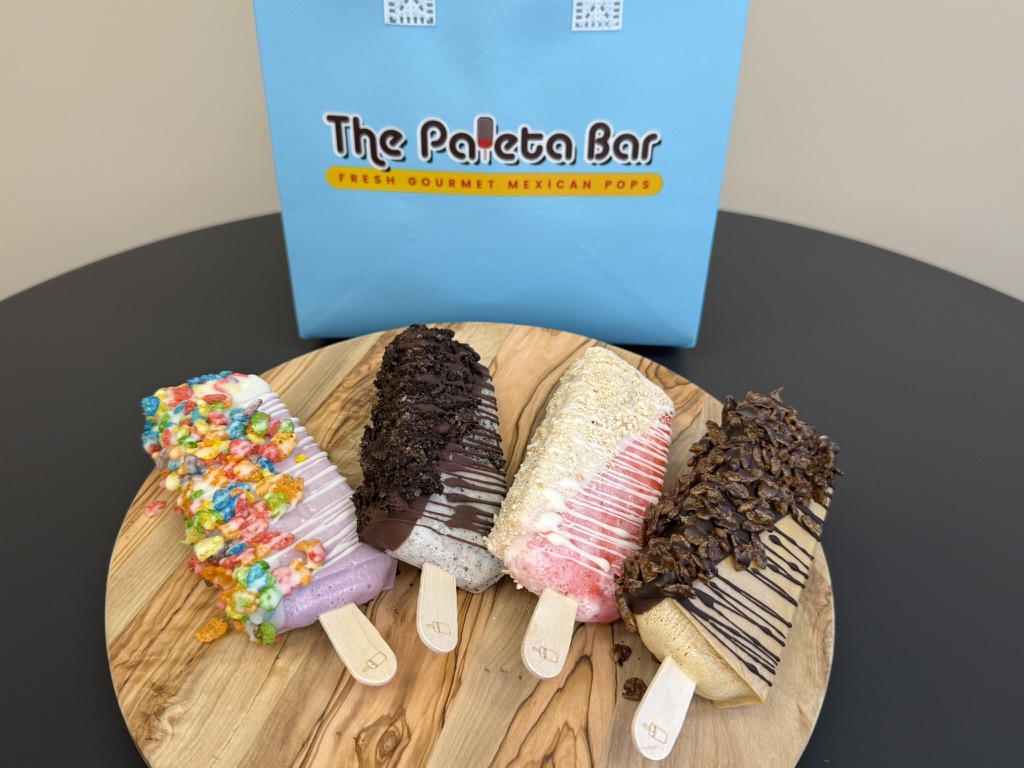 Four dipped paletas on a board with a Paleta Bar gift bag